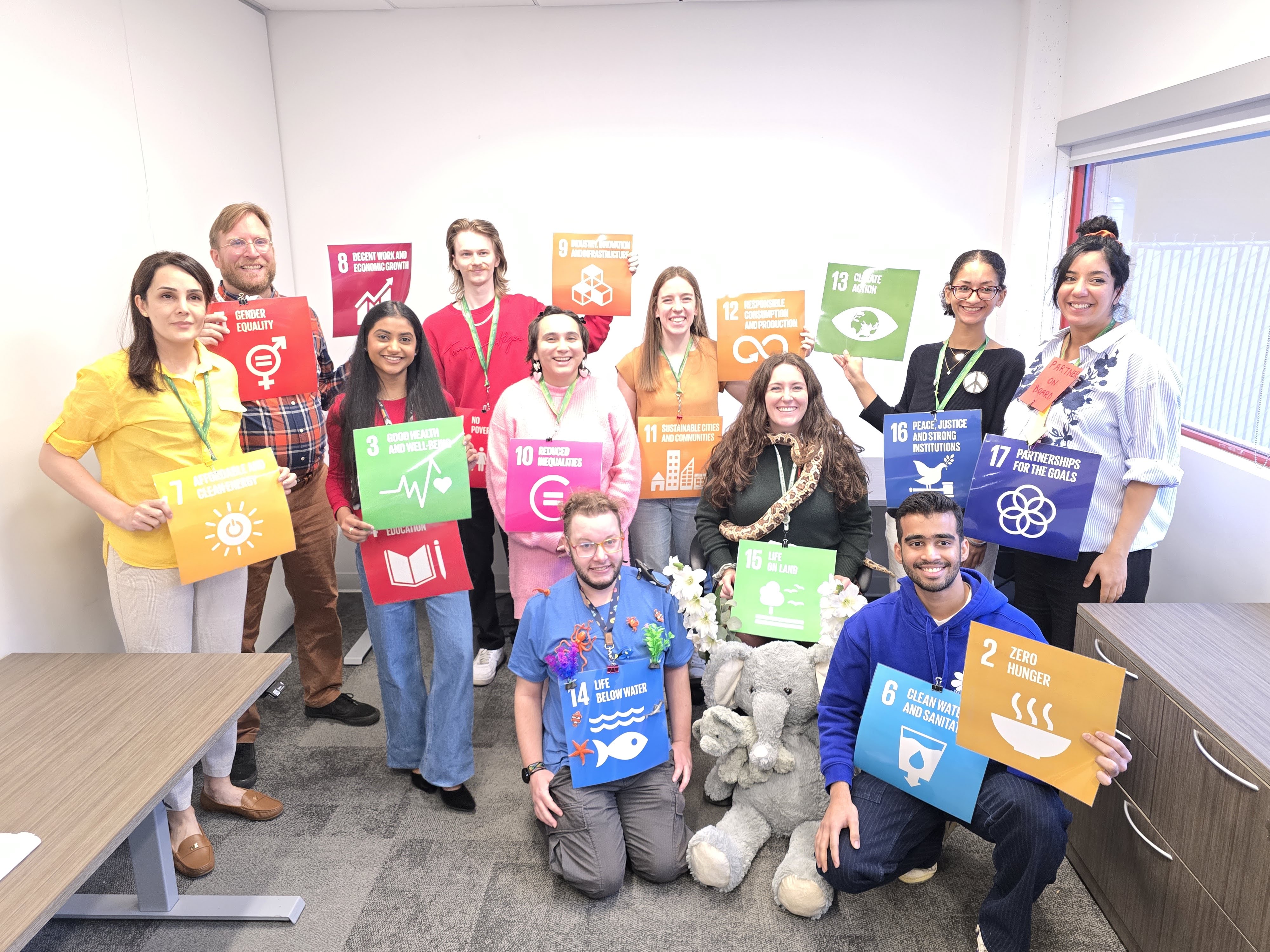 11 team members of the office of sustainability smile at the camera holding up the symbols for the united nations sustainable development goals